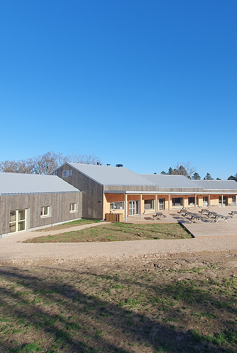 Bâtiment en bois moderne avec terrasse extérieure aménagée, sous un ciel dégagé.