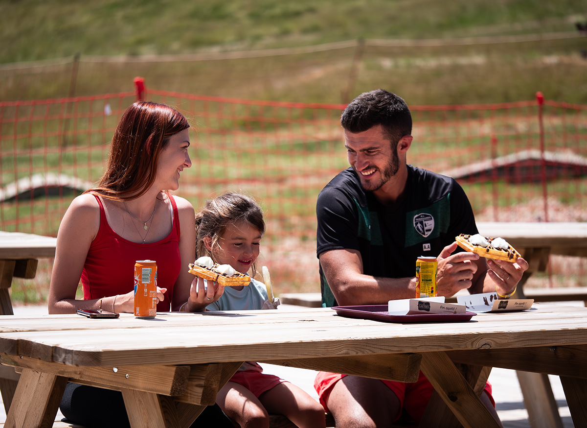 Famille attablée en plein air savourant des gaufres et des boissons fraîches sur une terrasse en bois au parc de Prabouré.
