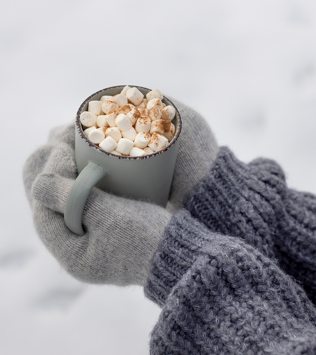 Mains gantées tenant une tasse de chocolat chaud avec des guimauves en hiver.